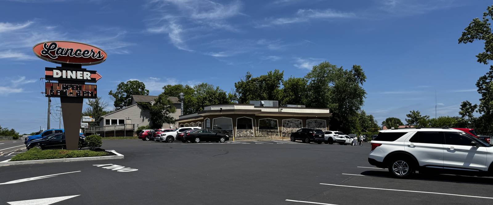 The red Lancers Diner sign by the road, with the diner and its parking lot behind it on a sunny day