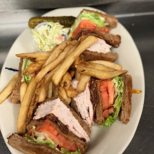 A triple-decker turkey club cut into quarters, with French fries, coleslaw and a pickle
