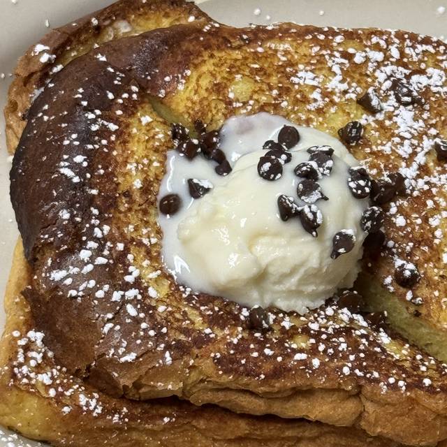 Thick-cut French toast dusted with powdered sugar, topped with cream and chocolate chips