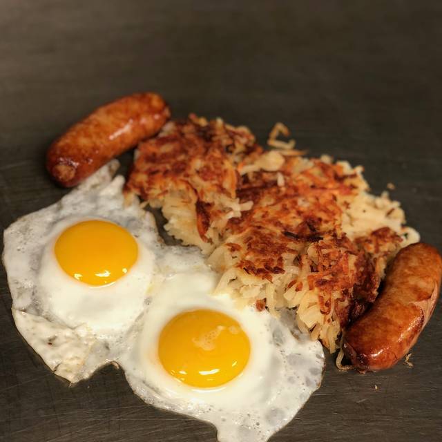 Two sunny-side-up eggs with crispy home fries and sausage links on the griddle