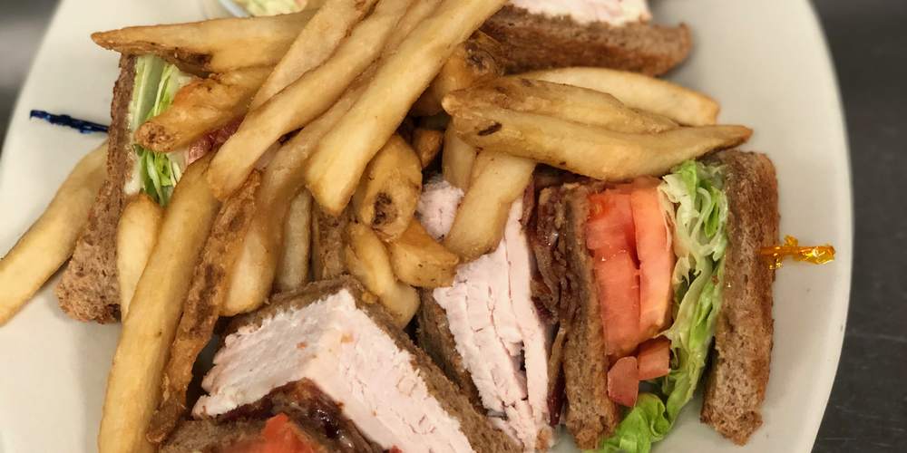 A triple-decker turkey club on wheat toast, cut into quarters, with French fries