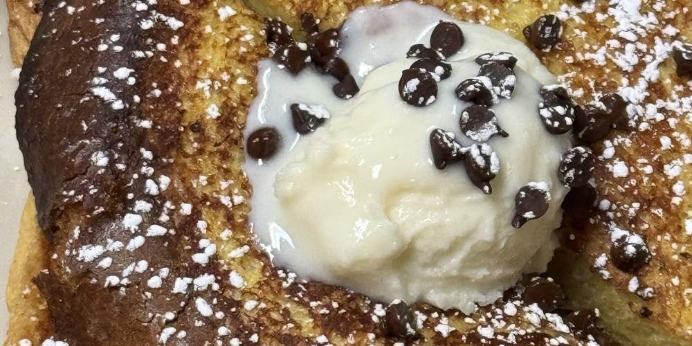 Thick-cut French toast dusted with powdered sugar, topped with cream and chocolate chips