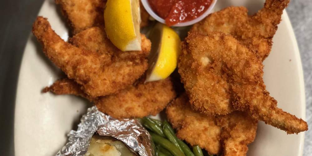 Golden fried jumbo shrimp with lemon wedges, cocktail sauce, green beans and a baked potato
