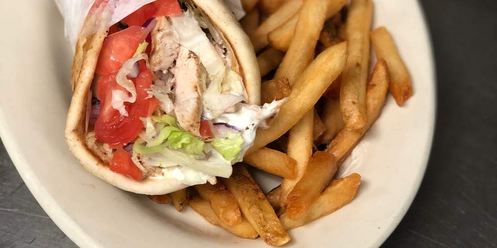 A grilled chicken gyro in pita with lettuce, tomato and tzatziki, with French fries