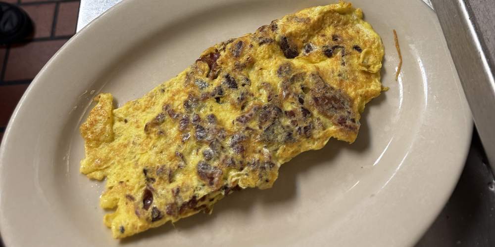 A folded omelet with sausage and onions on a diner plate