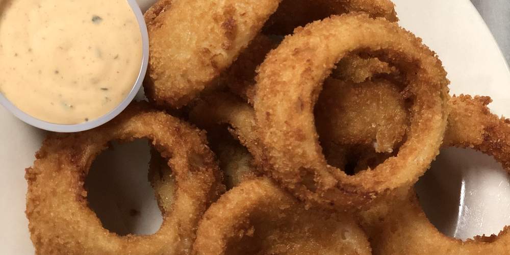Breaded onion rings piled on a plate with a cup of dipping sauce