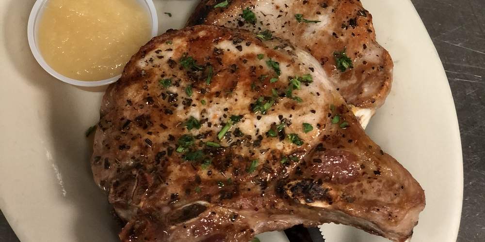 Two thick-cut pork chops with applesauce and a baked potato