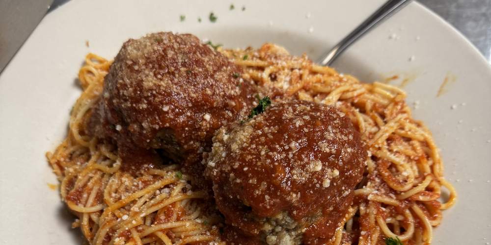 Spaghetti with two meatballs in red sauce, topped with grated cheese