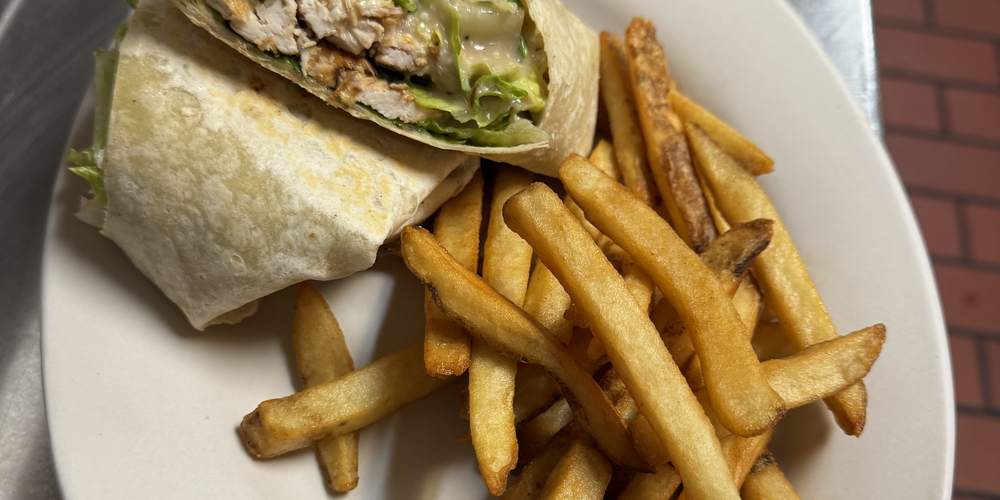 A grilled chicken wrap cut in half, served with French fries